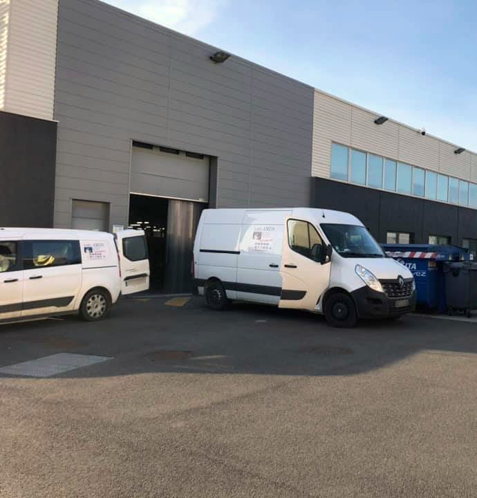 Deux véhicules blancs garés devant la porte d'un bâtiment industriel.