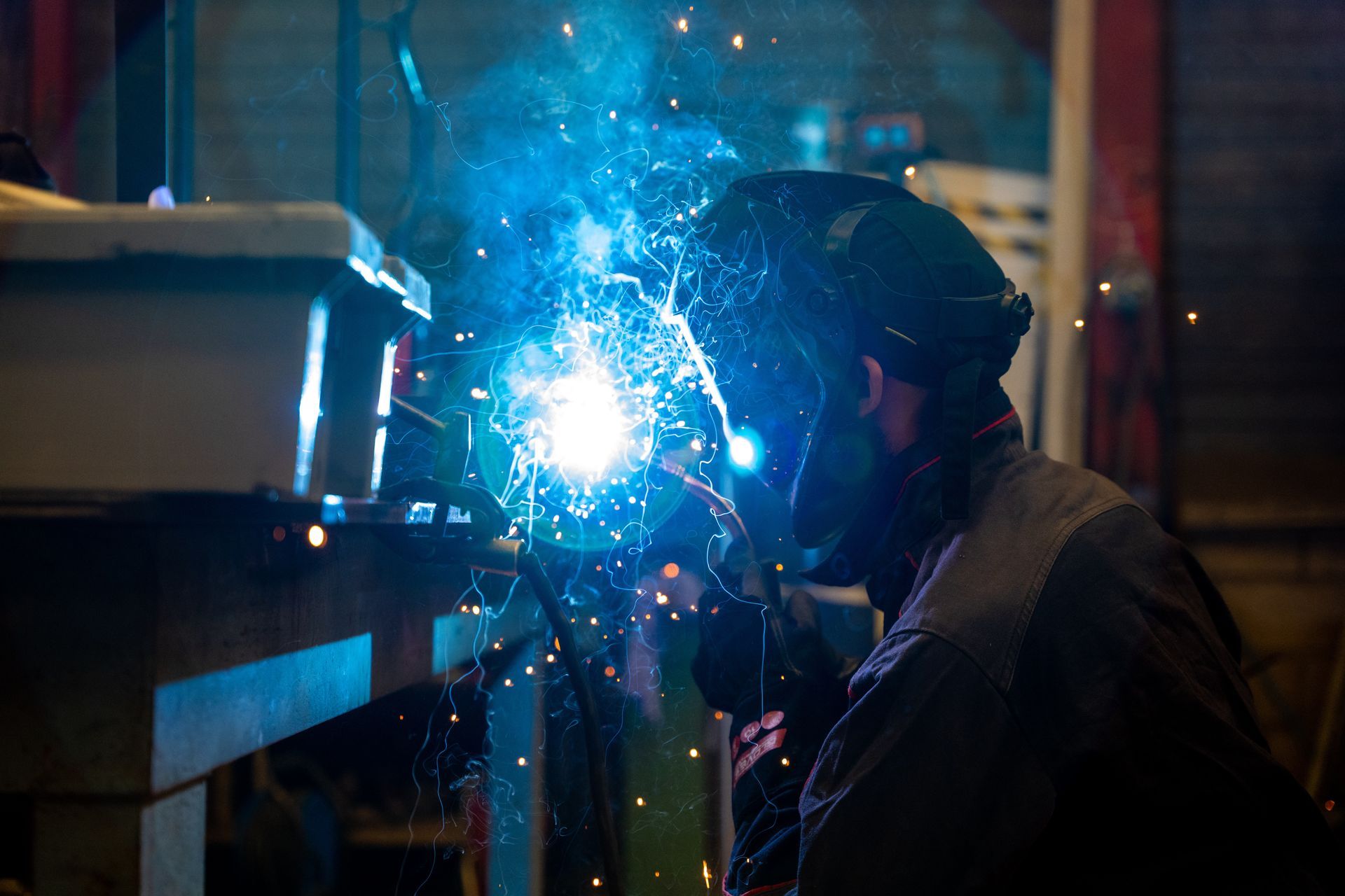 Ouvrier portant un casque à soudure en train de souder une pièce 