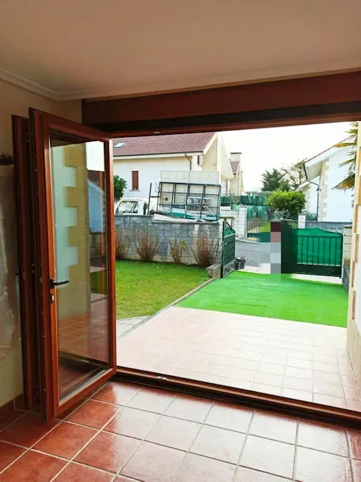 Puertas francesas de madera abiertas que conducen desde una habitación con piso de baldosas a un patio trasero con césped verde y vista a la calle.