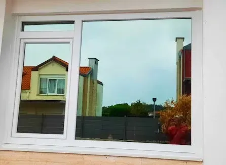 Ventana con marco blanco que refleja casas, cielo gris y follaje otoñal.