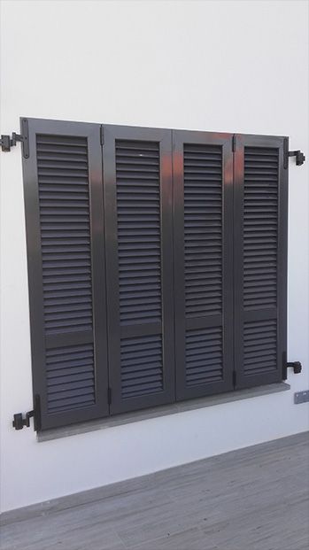 Contraventanas grises cerradas en un edificio blanco, fijadas con bisagras y abrazaderas.