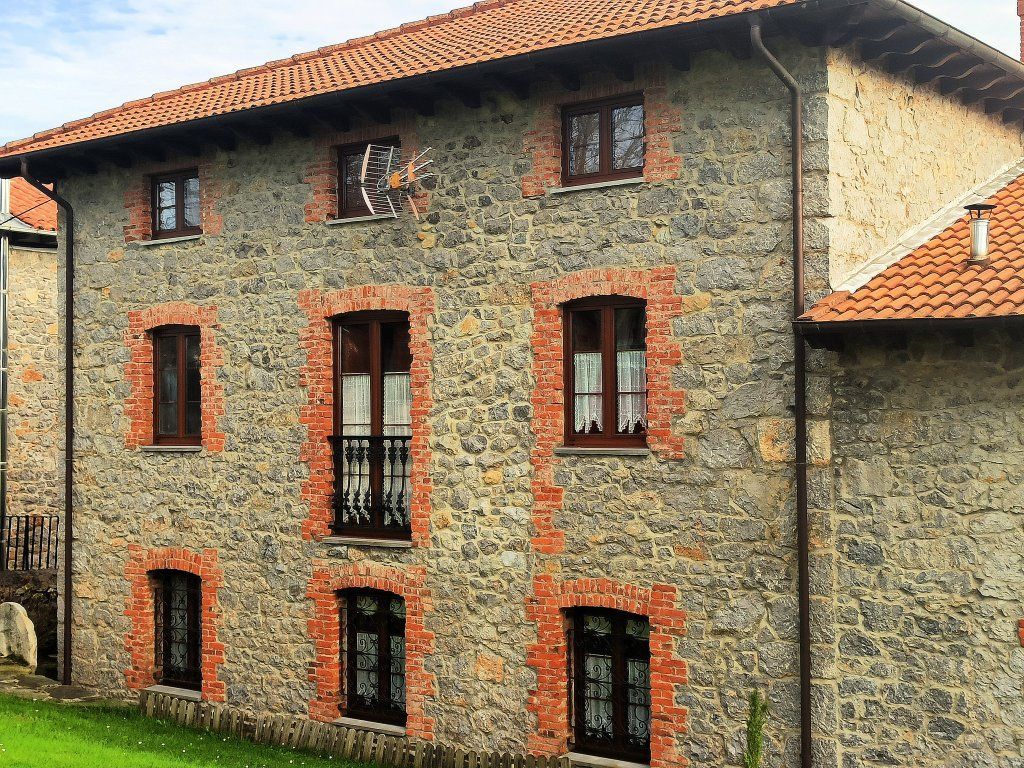 Edificio de piedra de dos pisos con techo de tejas rojas, molduras de ladrillo alrededor de las ventanas y marcos de ventanas de color marrón oscuro.