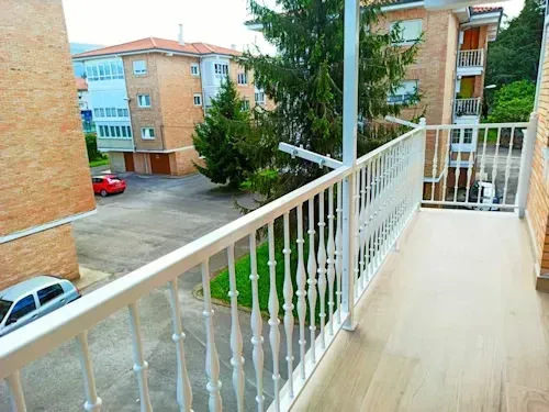 Balcón con barandillas blancas con vista a un patio con edificios de departamentos y autos.