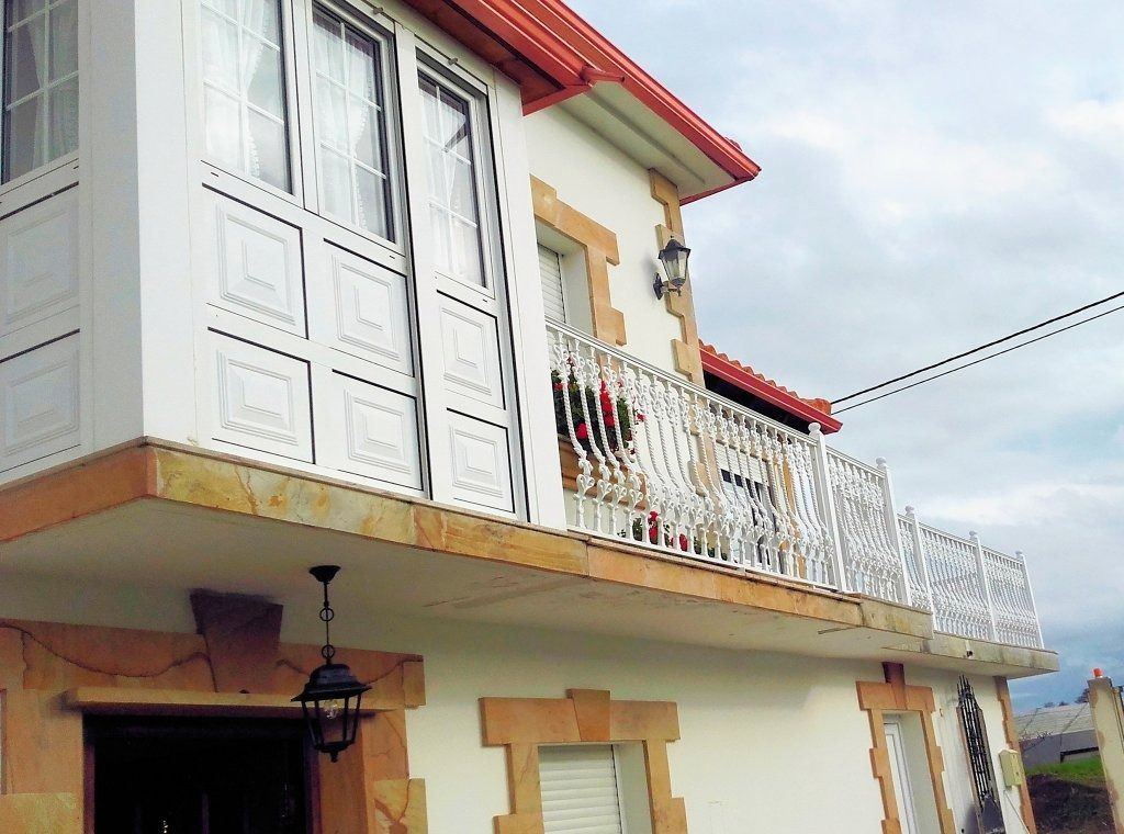 Casa blanca con techo y molduras naranjas, con un balcón con una barandilla blanca ornamentada. Un farol cuelga bajo el balcón.