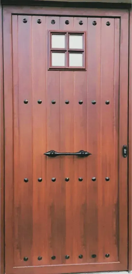 Puerta de madera con una pequeña ventana, detalles tachonados y tirador decorativo.