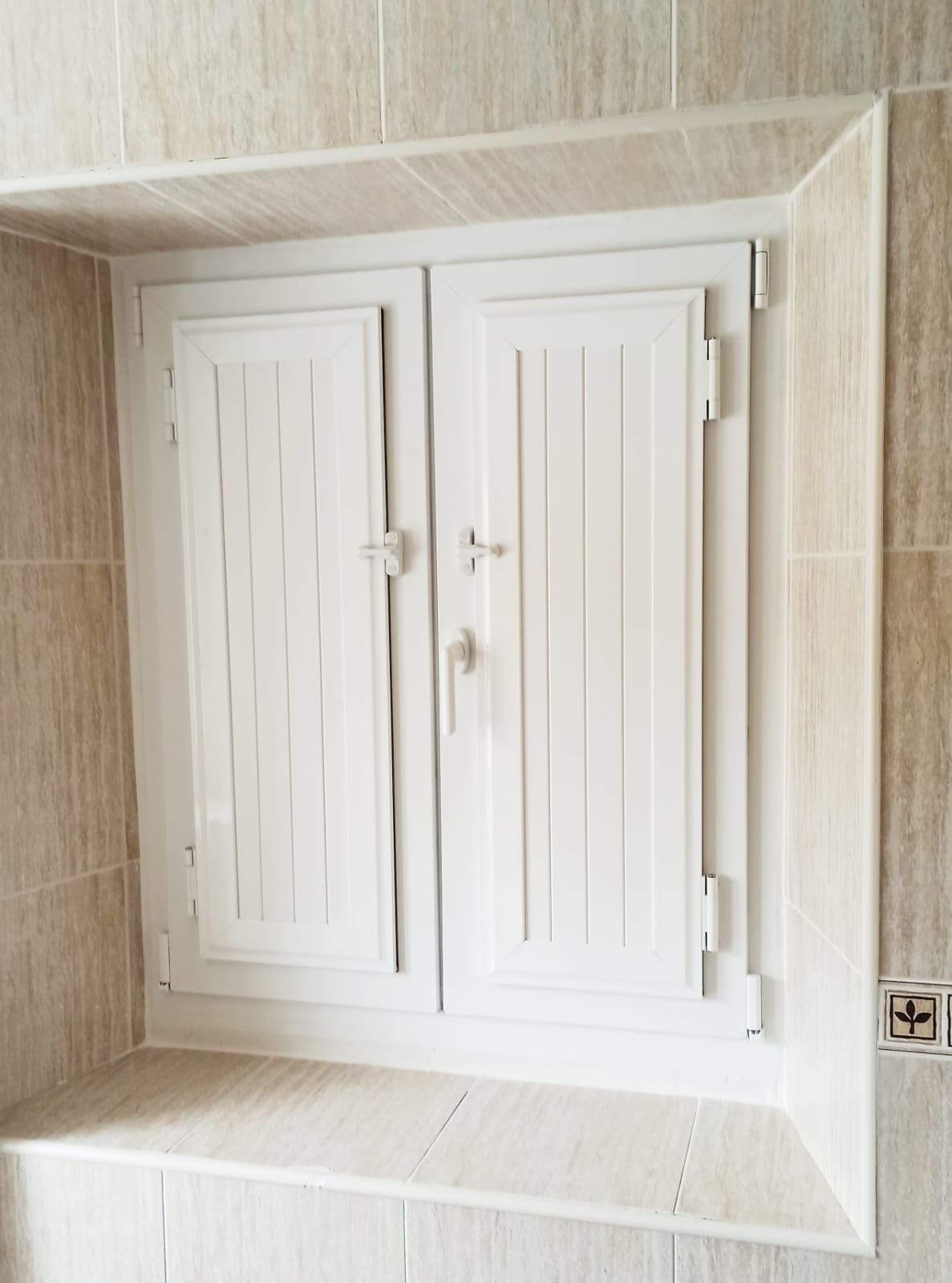 Puertas de armario con lamas blancas, integradas en una pared de azulejos. Las puertas tienen tirador y cerradura.