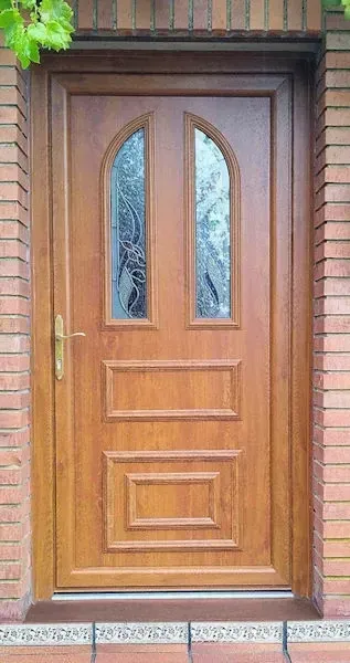 Puerta de madera con dos paneles de vidrio arqueados y dos paneles rectangulares, colocados en un marco de ladrillo.