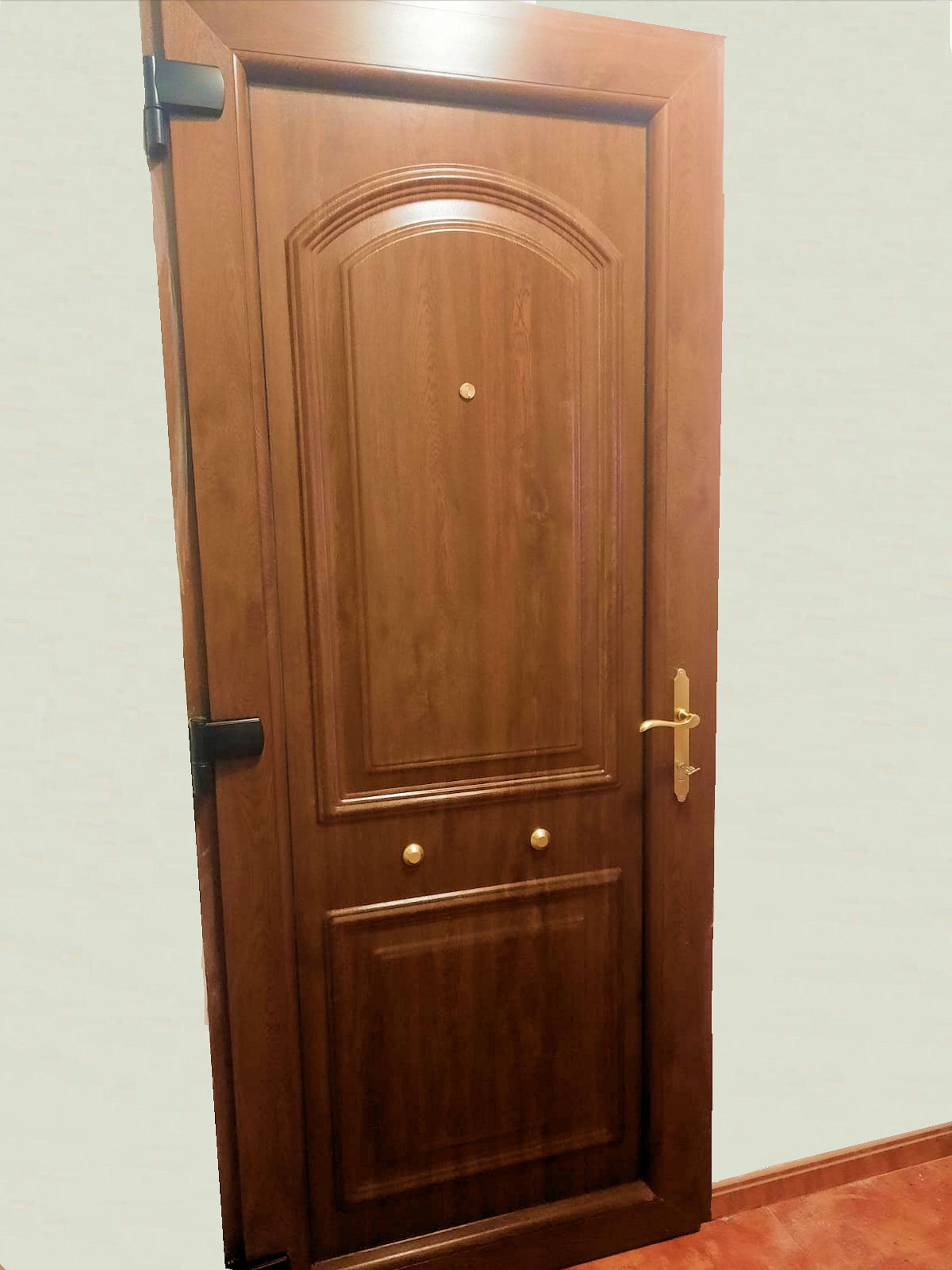 Puerta interior de madera con panel superior arqueado, herrajes de latón y mirilla.