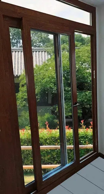 Las puertas corredizas de vidrio con marco marrón conducen a un jardín con árboles verdes y flores rojas.