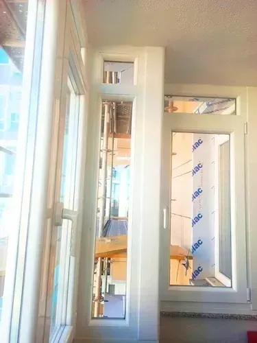 Ventanas con marco blanco en un balcón, una abierta, con vista a un área en construcción.