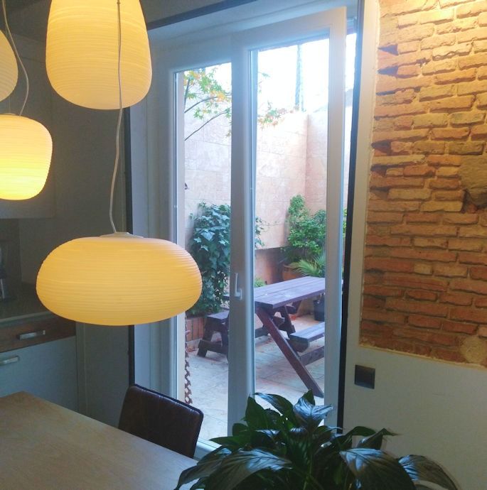 Un comedor con luces colgantes y vista a un pequeño patio al aire libre con mesa de picnic y plantas.