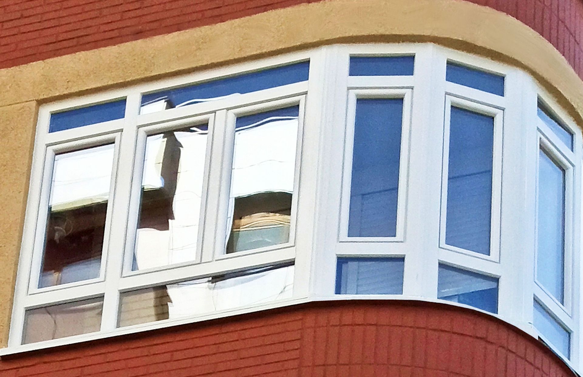 Un ventanal con marcos blancos, ubicado en un edificio de ladrillo rojo con una esquina curva de color beige.