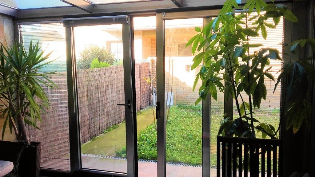 Terraza acristalada con puertas corredizas de vidrio abiertas que dan a un pequeño patio con cerca de bambú y césped verde.