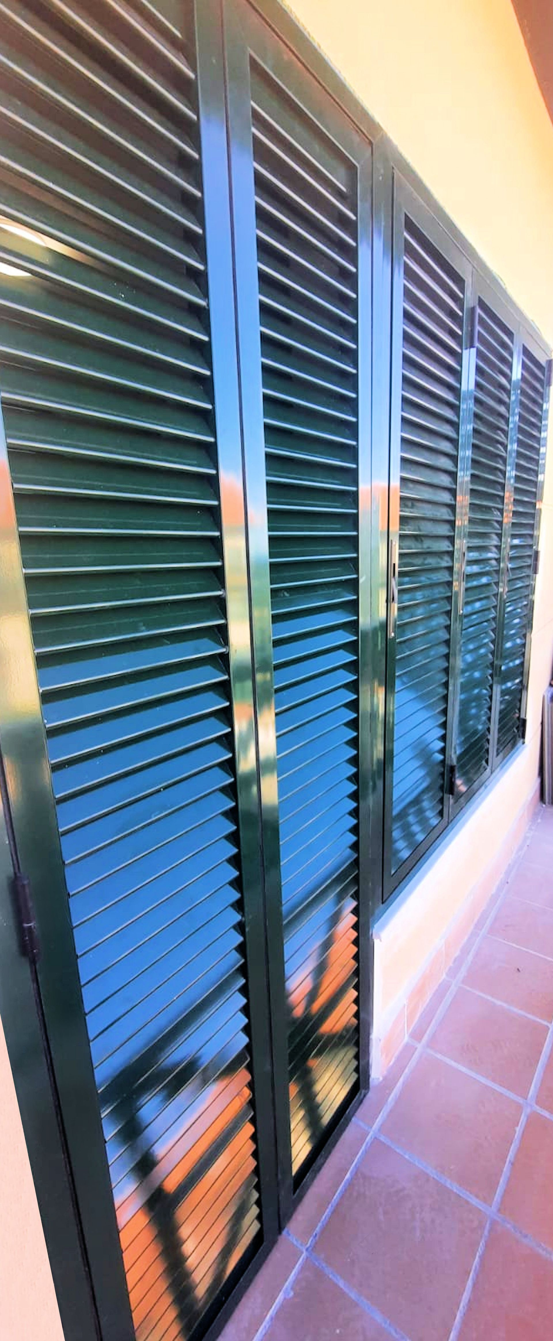 Contraventanas verdes en un patio de baldosas. Las contraventanas están cerradas y reflejan el entorno.