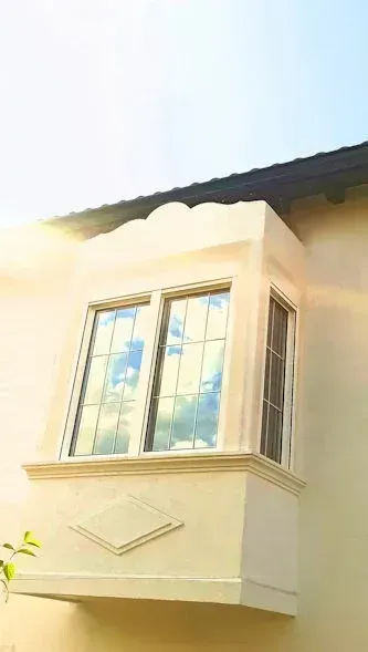 Ventanal con fachada de estuco beige, que refleja un cielo azul con nubes.