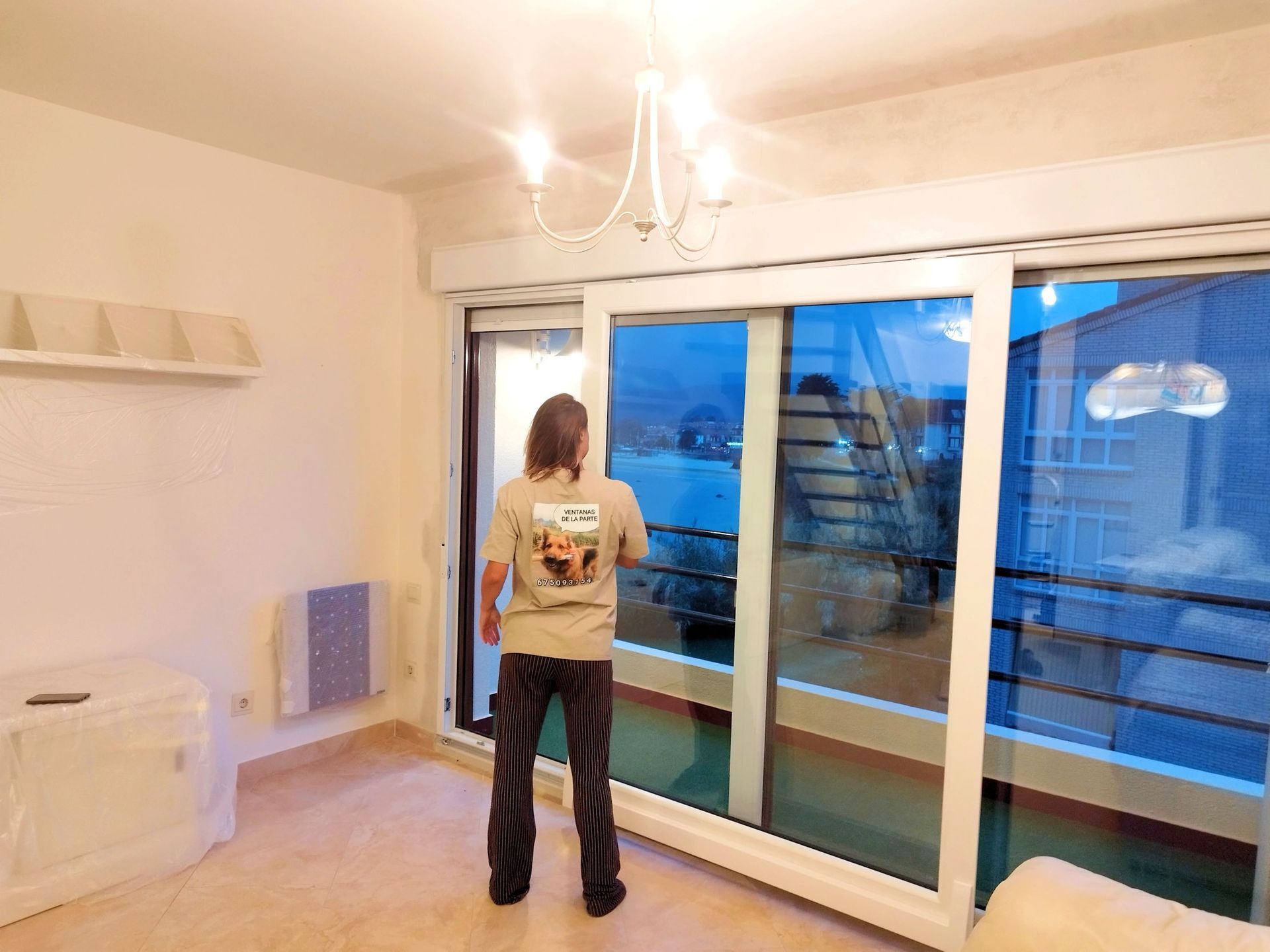 Persona de pie junto a unas puertas corredizas de cristal abiertas, mirando a un balcón con vistas nocturnas. Se encuentra en un apartamento.
