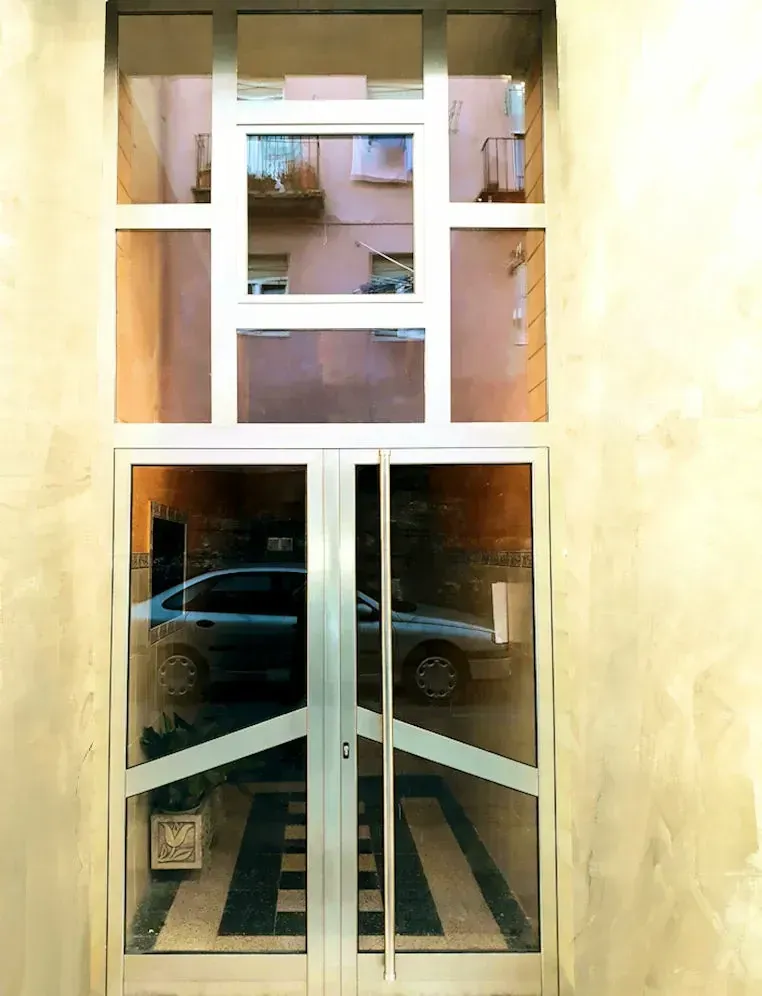 Puertas dobles de vidrio con un automóvil visible en el interior, debajo de una sección de ventana con otros edificios a la vista.