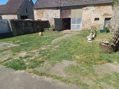 Cour intérieure en pierre d'une ferme, avec un jardin gazonné clairsemé, une haie et des plantes en pot près de la porte.