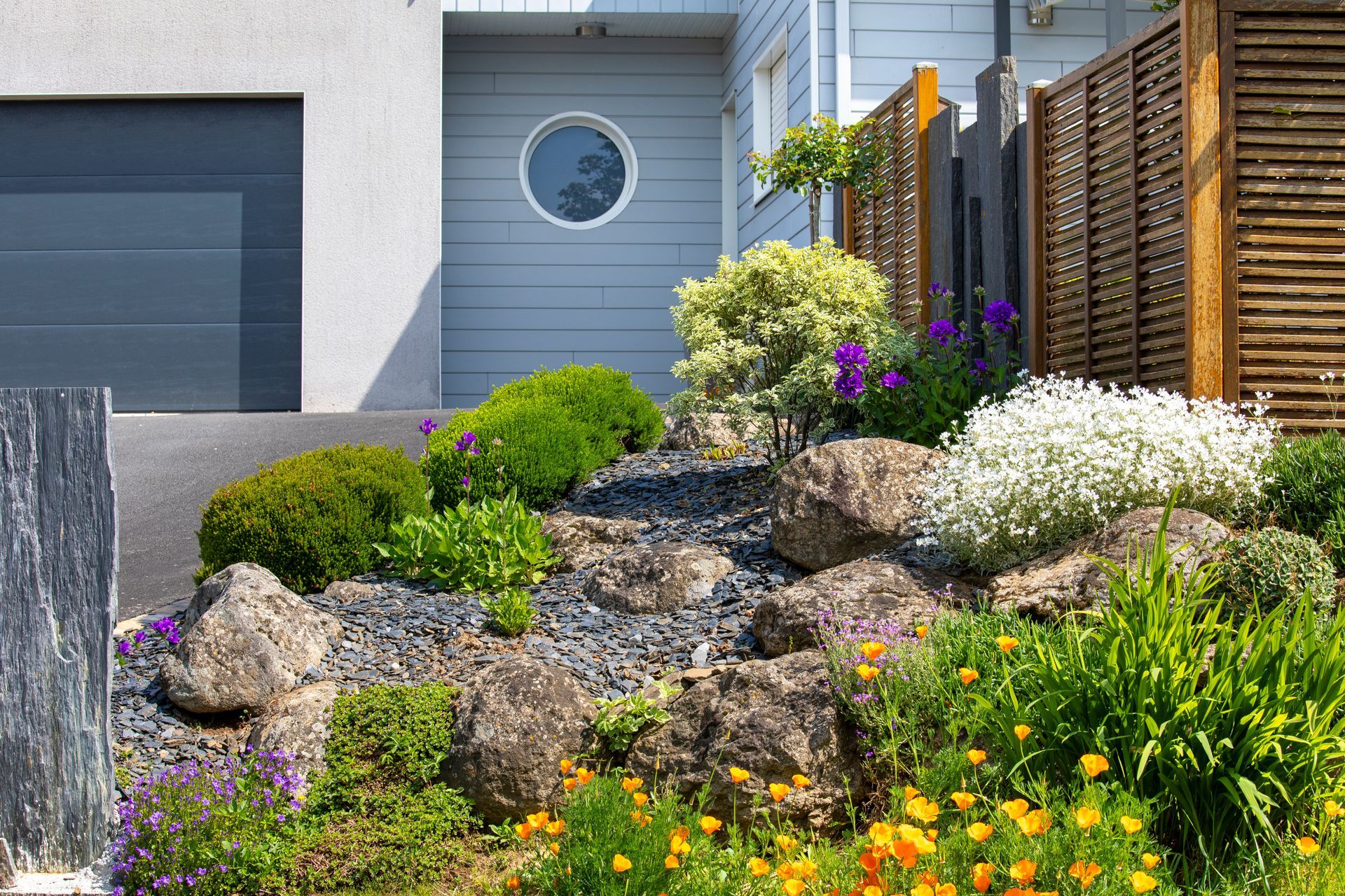 Jardin de rocaille avec arbustes fleuris à l'avant d'une maison moderne et d'un garage.