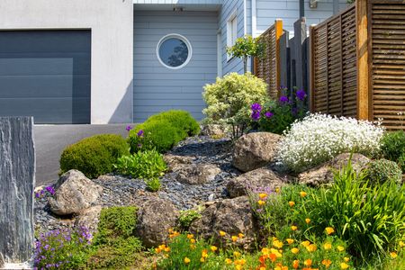 Jardin de rocaille avec arbustes fleuris à l'avant d'une maison moderne et d'un garage.