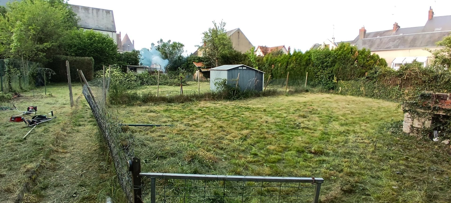 Jardin arrière avec pelouse, haies, clôture et abris de jardin sous un ciel nuageux