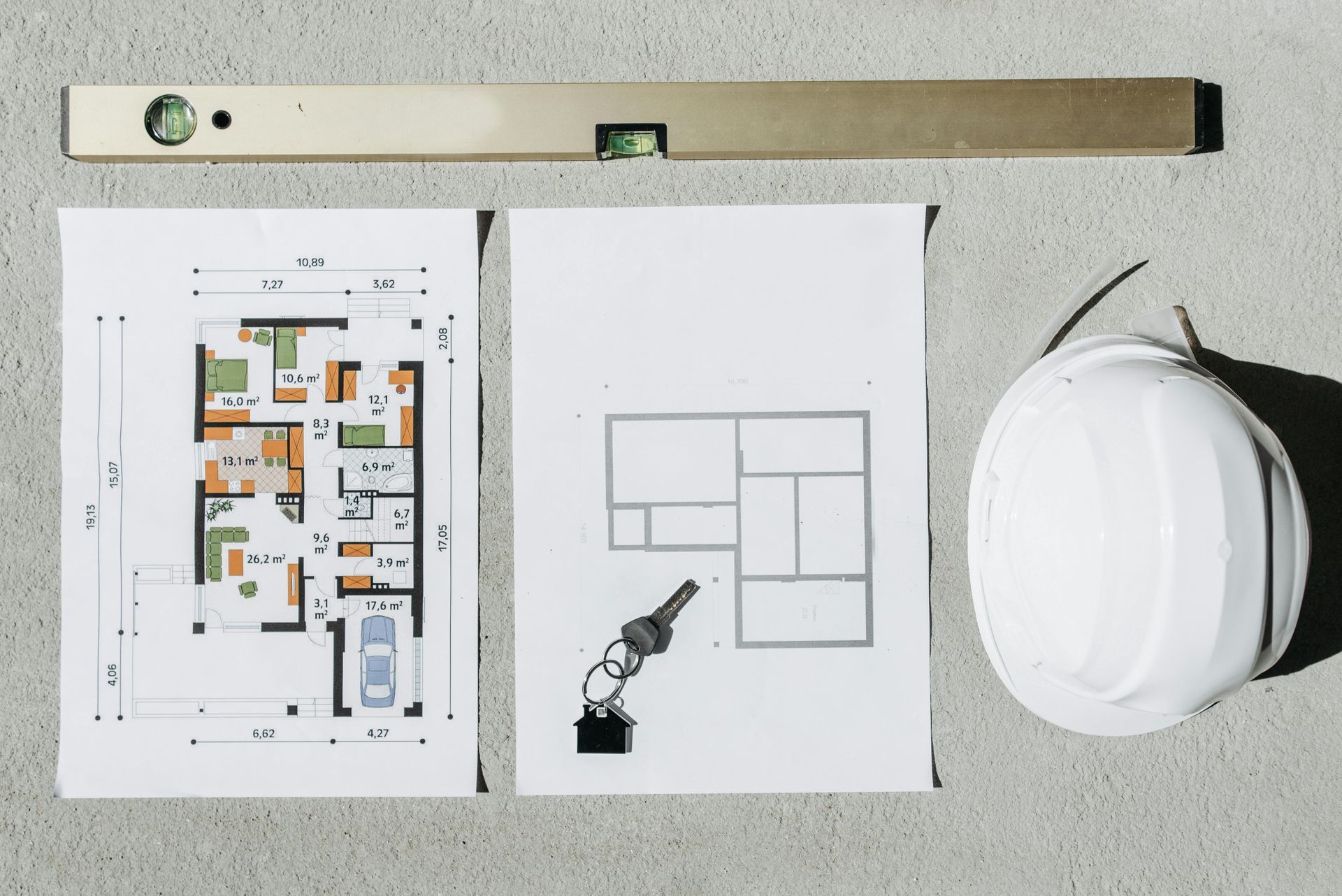 Sobre una mesa hay un dibujo de una casa, un nivel y un casco.