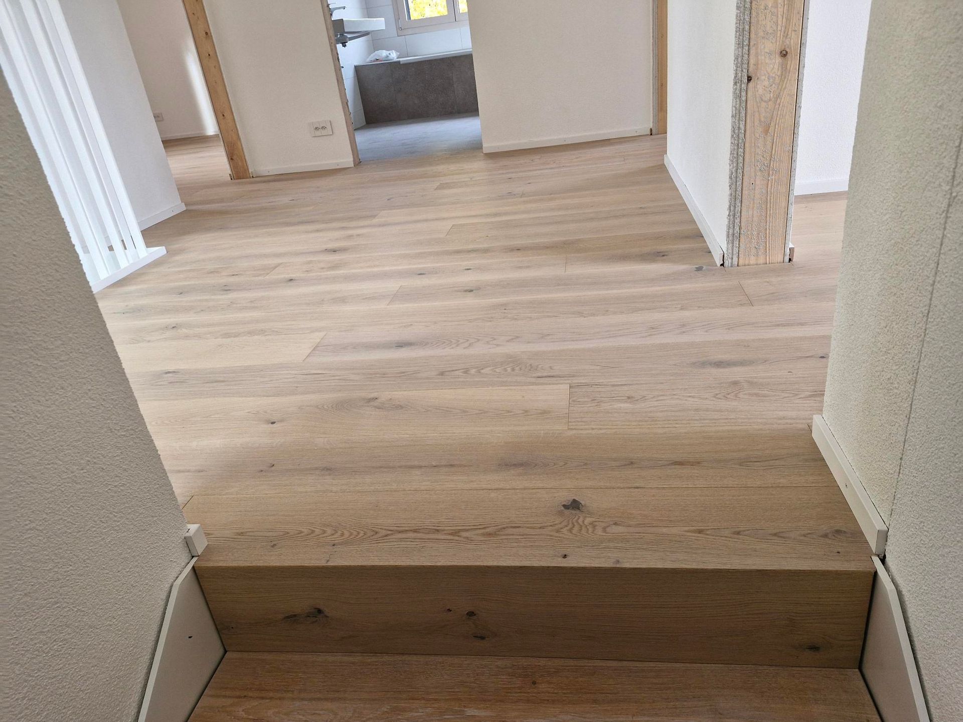 Une marche menant à une pièce intérieure avec un parquet clair et des murs blancs.