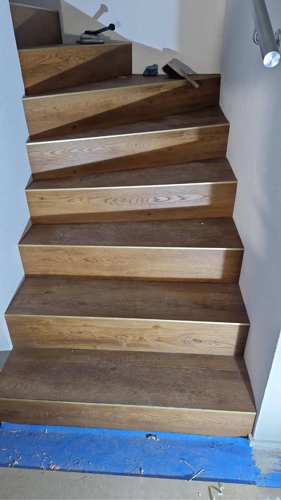 Un escalier aux marches et contremarches en bois foncé, avec du ruban adhésif de protection bleu visible à sa base.