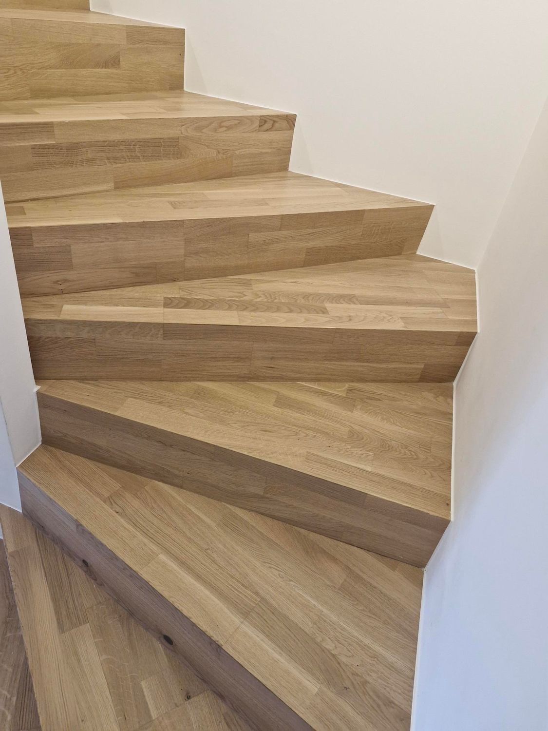 Escalier en bois avec marches sinueuses en forme de coin et murs blancs de part et d'autre.