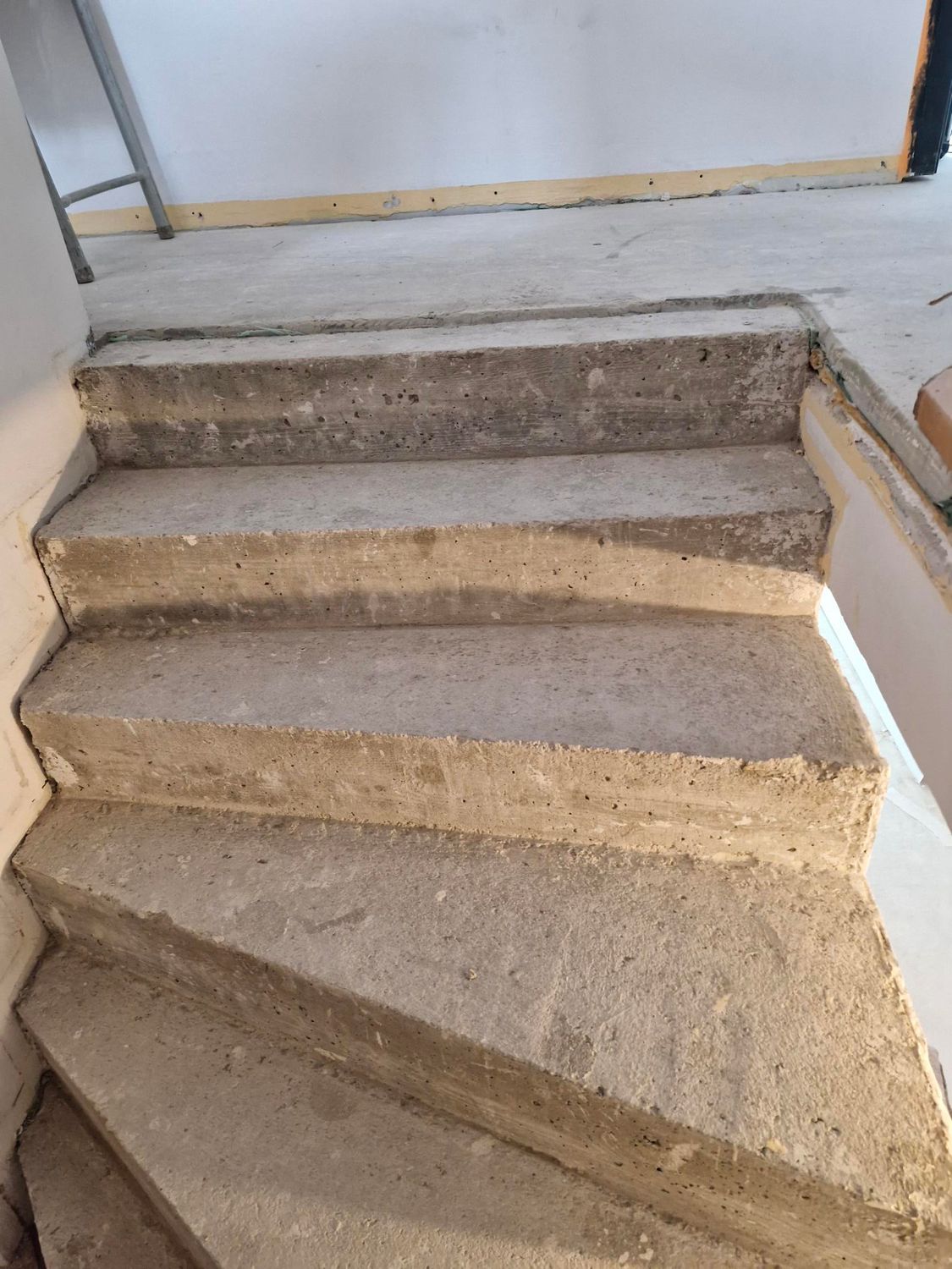 Un escalier en béton gris brut menant vers un mur et un cadre de porte.