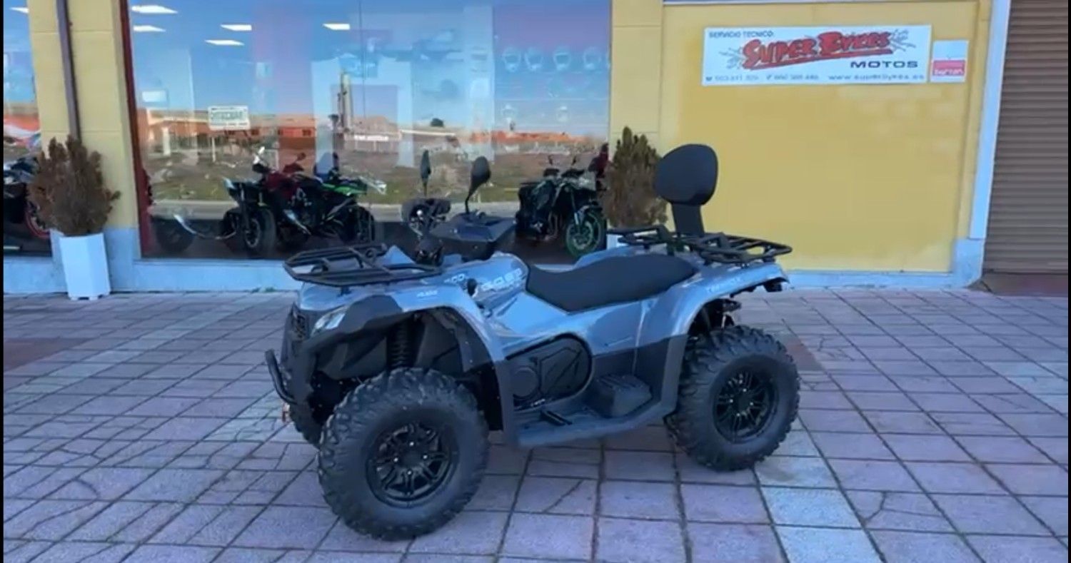 ATV CFMOTO gris con respaldo estacionado sobre el pavimento, otros vehículos borrosos en el fondo.