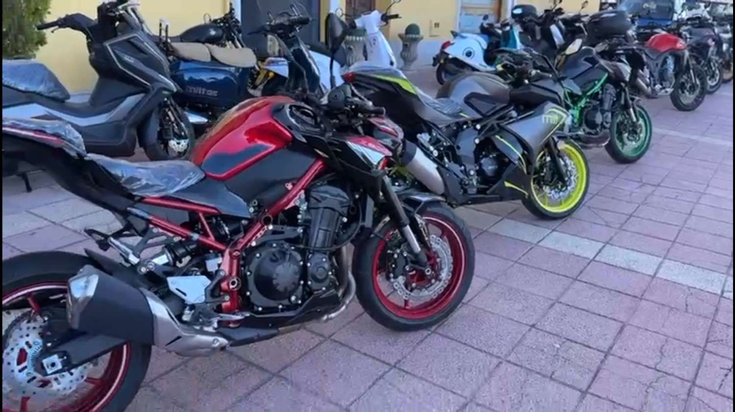 Motocicletas y scooters estacionados en fila afuera de un edificio.