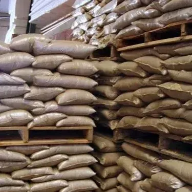 Pilas de sacos de arpillera, posiblemente llenos de grano, sobre paletas de madera en un almacén.