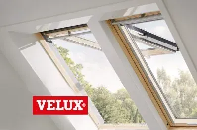 Dos tragaluces VELUX abiertos, enmarcados en madera, en ángulo en un techo blanco, con vista a los árboles.