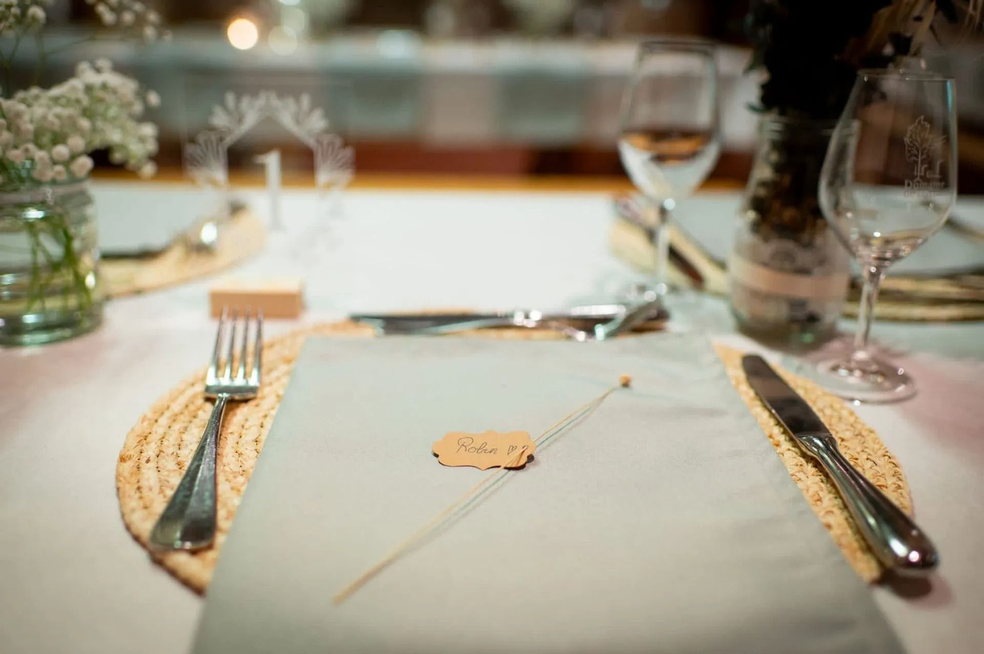 Couvre-lit avec serviette bleu clair, étiquette nominative, couverts et verres à vin.