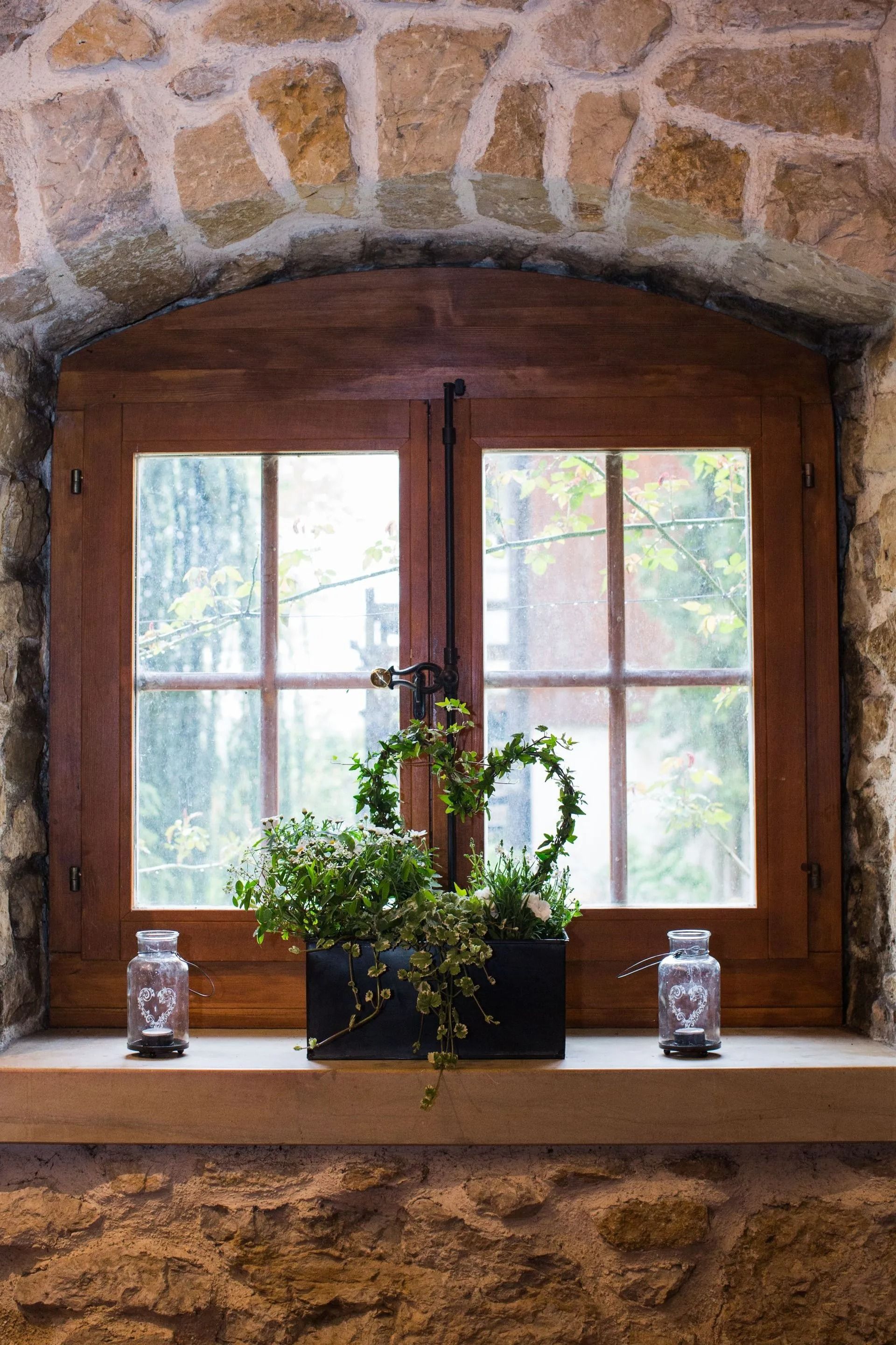 Fenêtre à cadre en bois et mur en pierre. Des plantes décoratives en pot sont posées sur le rebord de la fenêtre.