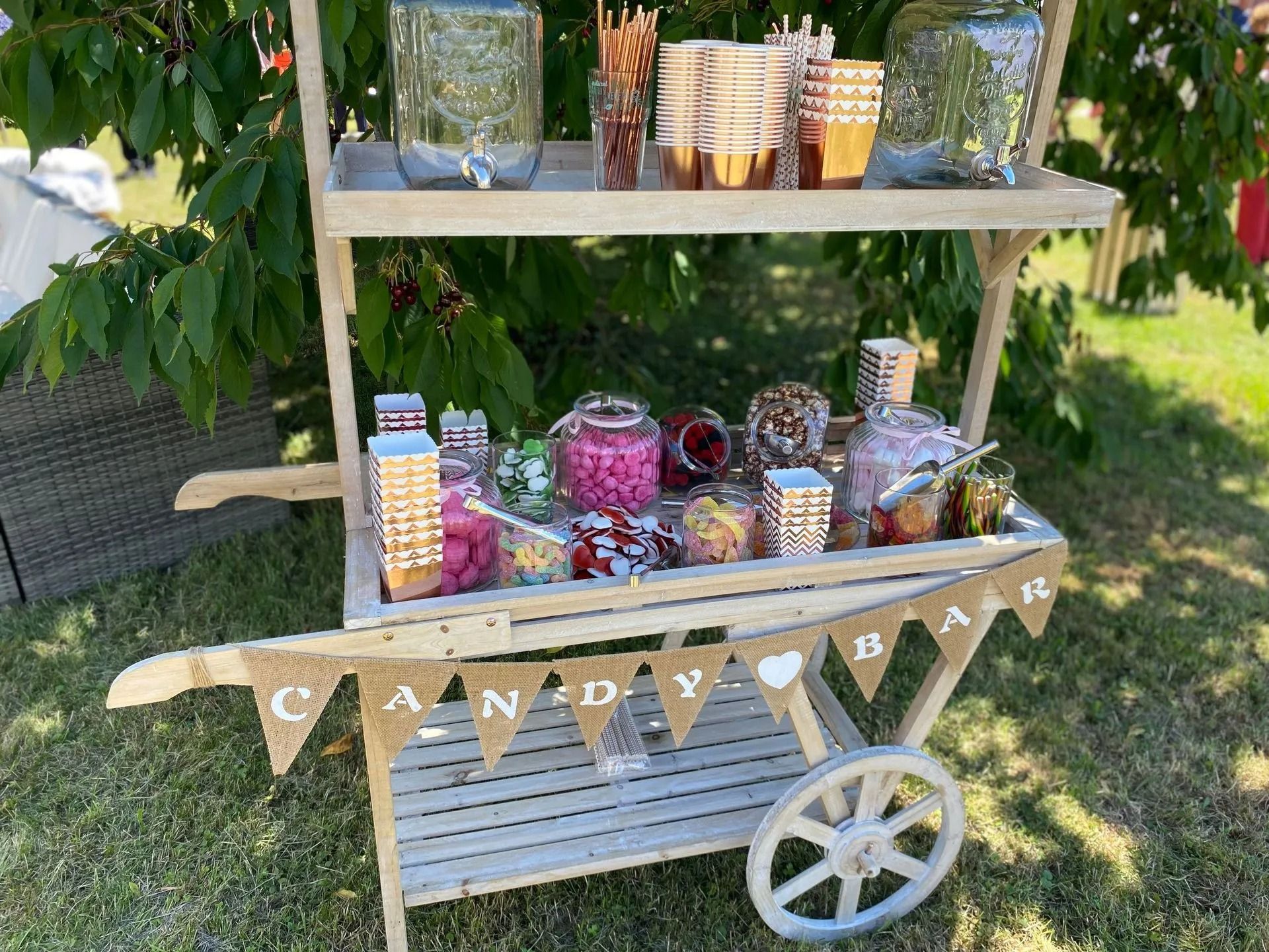 Chariot de bar à bonbons à l'extérieur, avec des friandises, des bocaux et une banderole « BAR À BONBONS ».