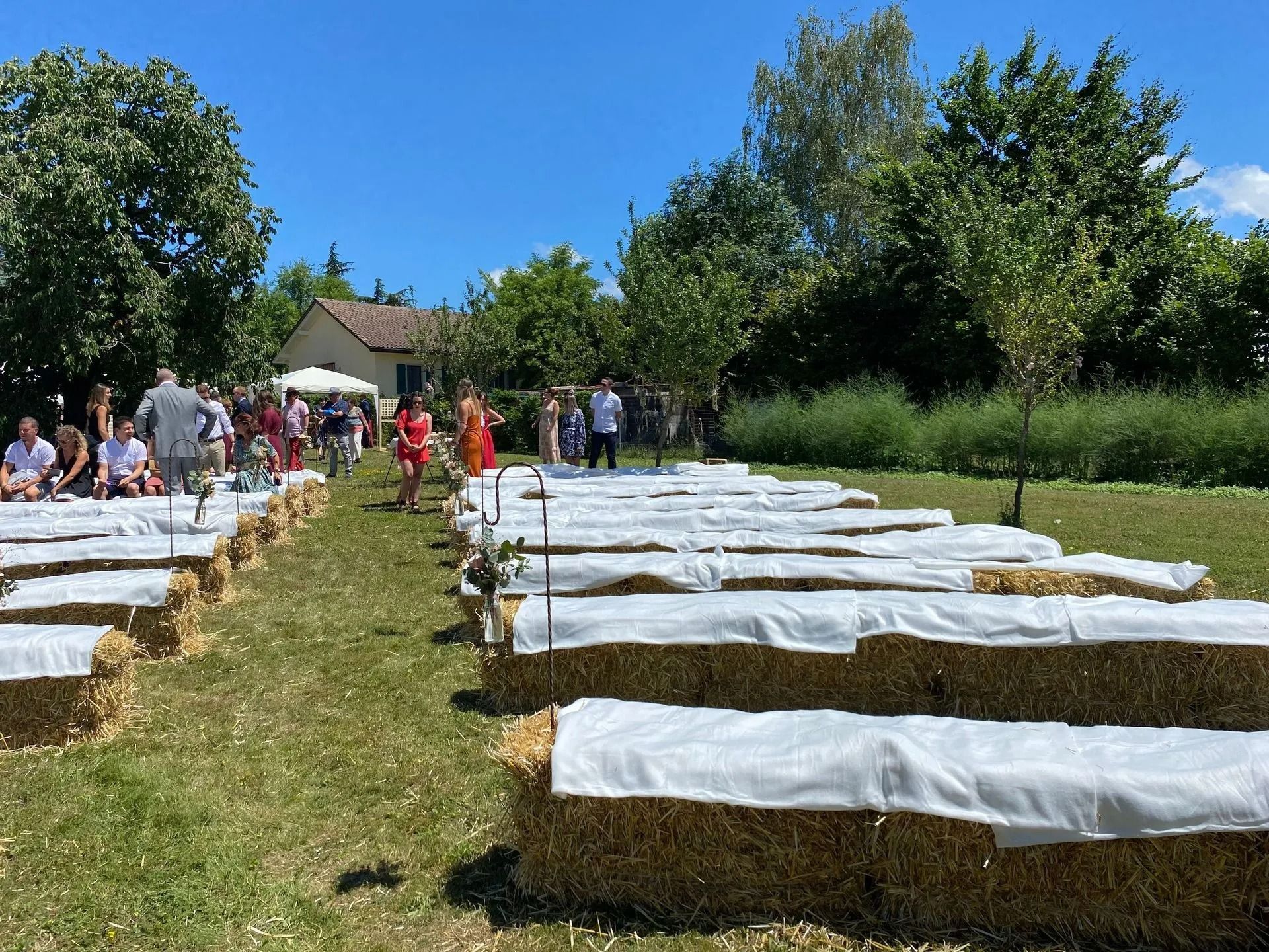 Cérémonie de mariage en plein air avec des sièges en bottes de paille, les invités réunis et une journée ensoleillée.