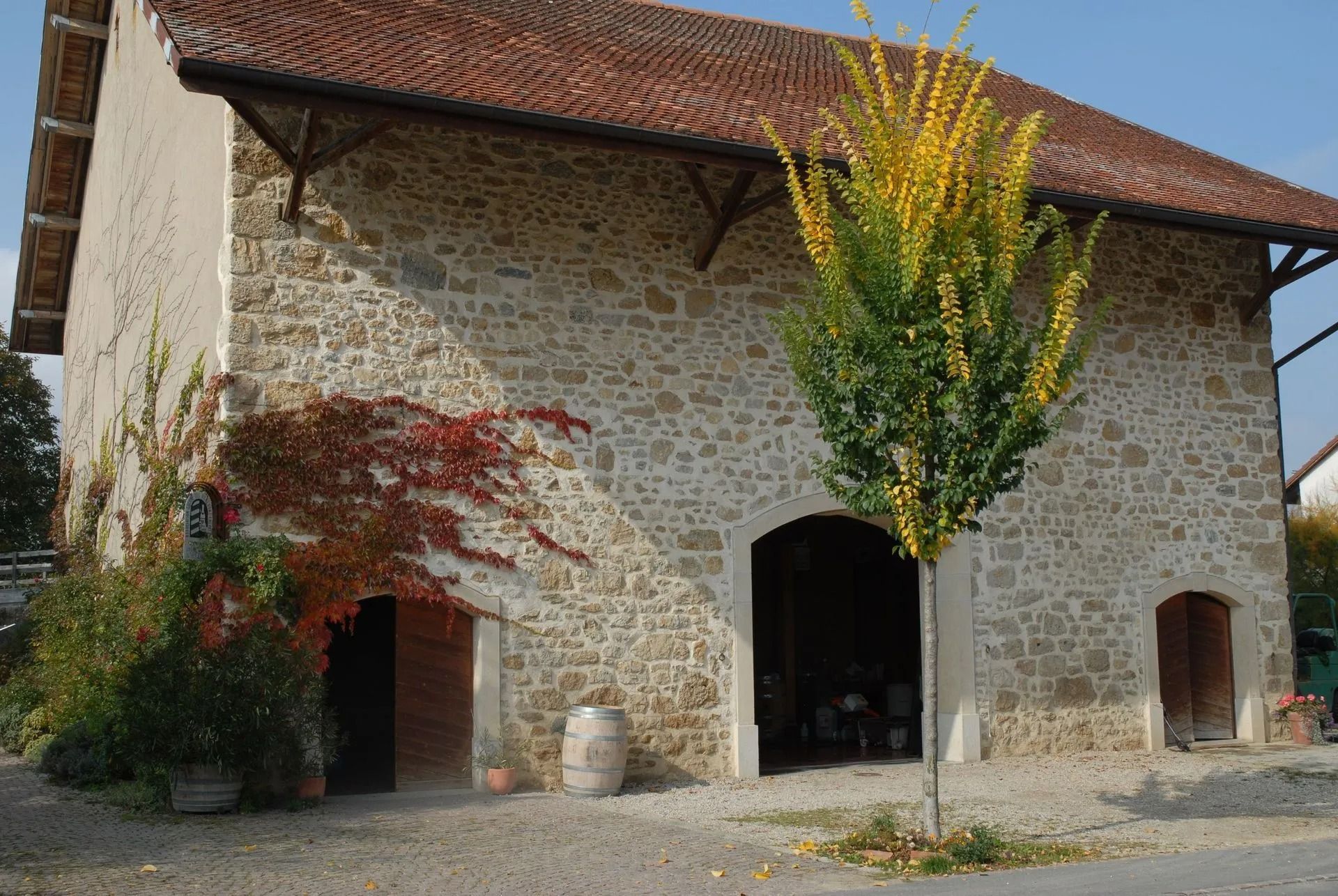 Bâtiment en pierre avec des ouvertures cintrées et un toit de tuiles, des arbres de chaque côté.