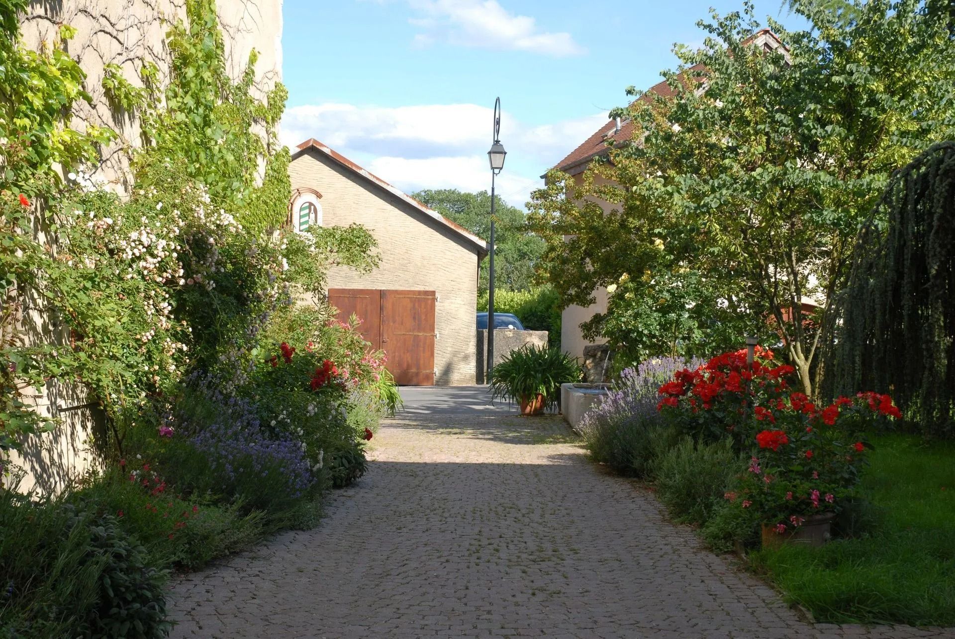 Chemin de pierre menant à des bâtiments bordés de fleurs et de verdure.