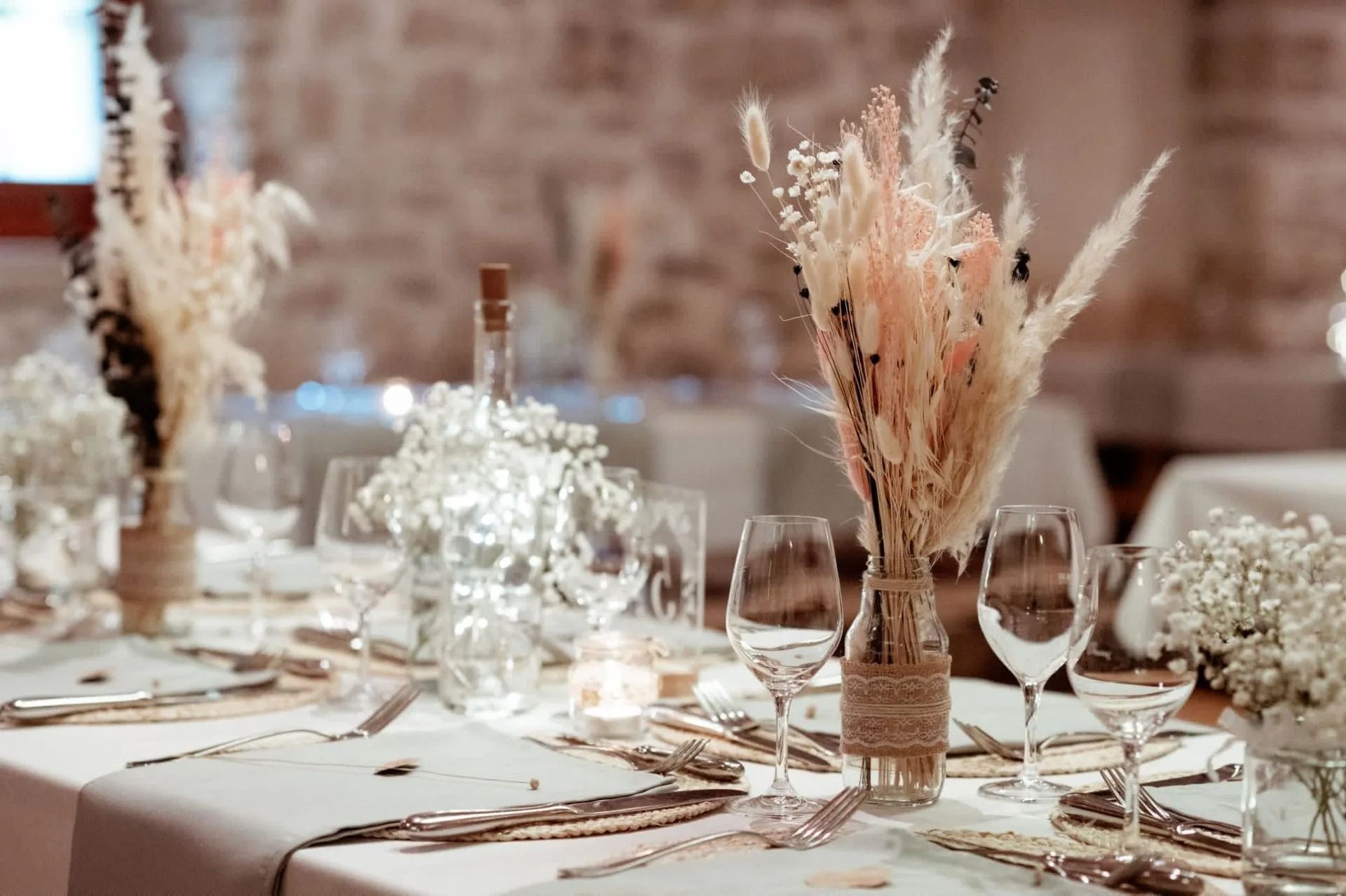 Mise en place de la table de réception de mariage avec compositions florales et verrerie.
