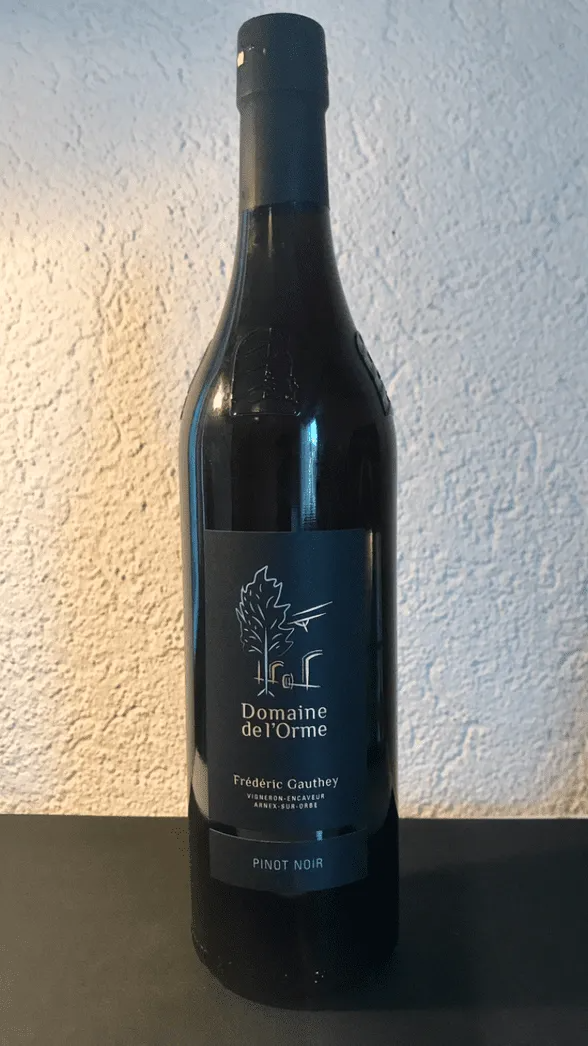 Bouteille de vin brun à l'étiquette noire, posée sur une surface sombre, contre un mur texturé.