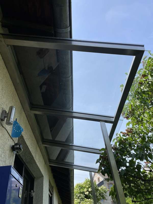 An der Seite eines Gebäudes befindet sich ein Vordach mit einem Dach aus klarem Glas.
