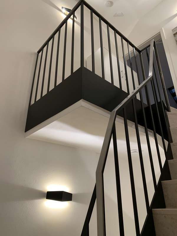 Eine Treppe mit schwarzem Geländer und einer Lampe an der Wand.