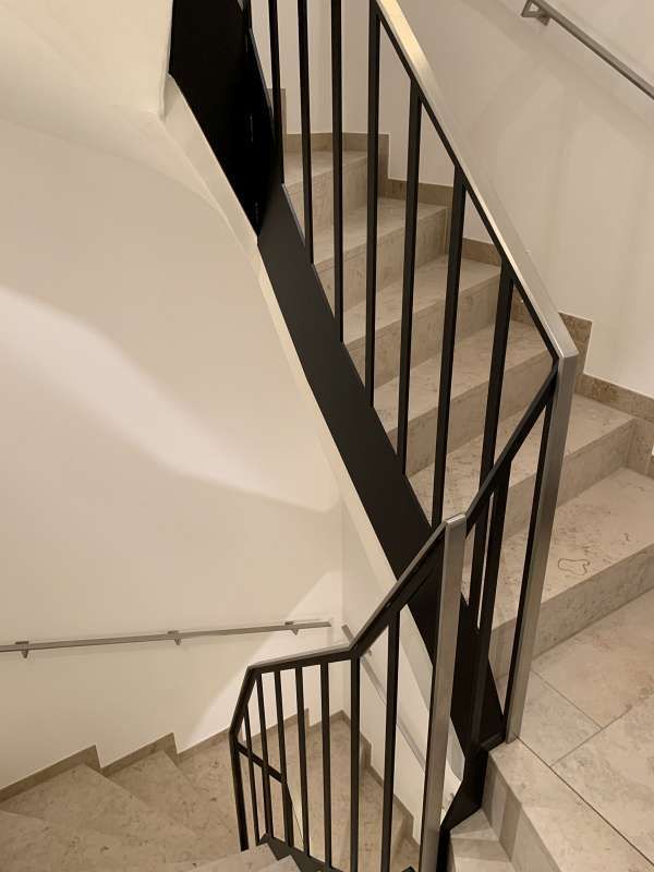 Eine Treppe mit schwarzem Geländer und weißer Wand