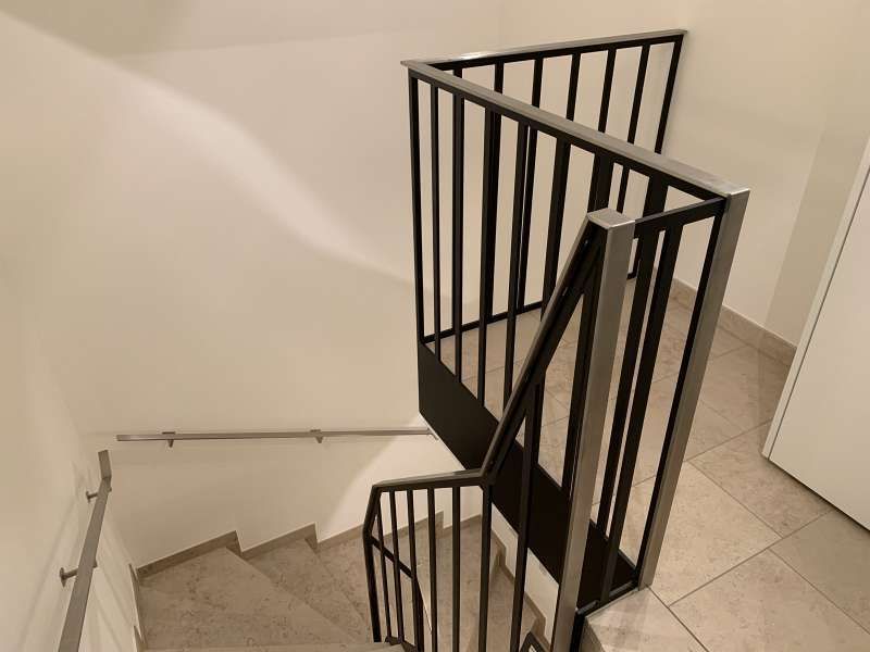 Eine Treppe mit schwarzem Geländer und weißer Wand.