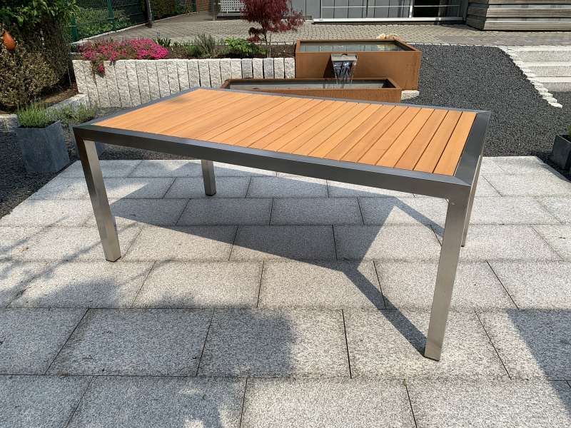 Ein Holztisch mit einem Edelstahlrahmen steht auf einer Terrasse