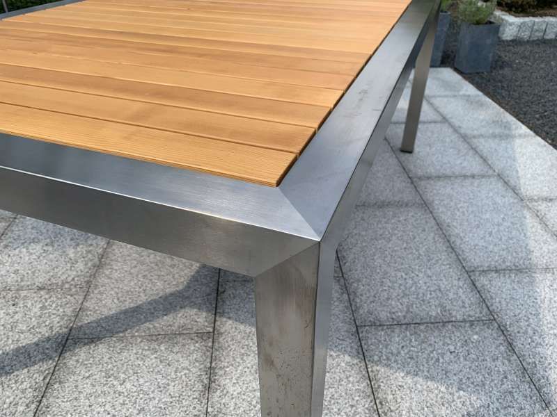 Ein Holztisch mit einem Edelstahlrahmen auf einer Terrasse