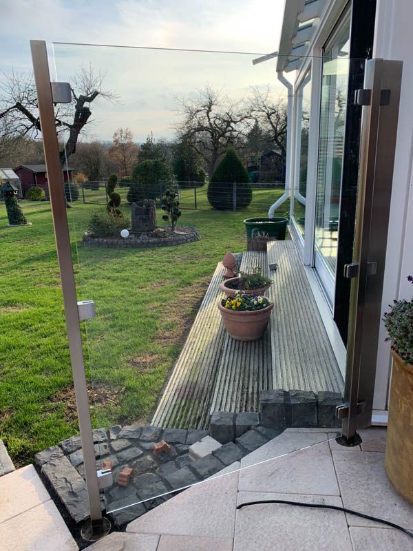 Eine Terrasse mit Glasgeländer und Topfpflanzen vor einem Haus.