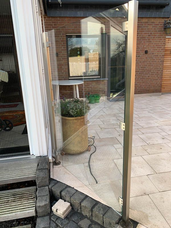 Eine Topfpflanze steht auf einer Terrasse neben einem Glaszaun.